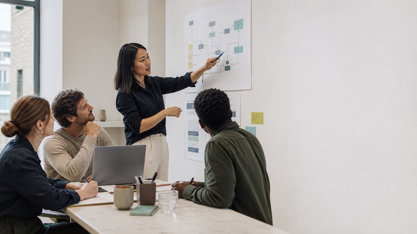 A team reviewing a data and reporting workflow diagram together on a whiteboard